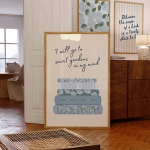 May include: A framed print featuring the quote "I will go to secret gardens in my mind" above a stack of blue books. Two other framed prints are visible, one with a floral pattern and another with vertical stripes and the text "Between the pages of a book is a lovely place to b."