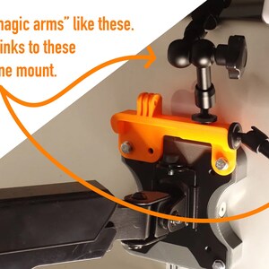 May include: Two black adjustable phone or camera mounts with a black and orange phone holder. The mounts are attached to a white surface. The text "But you need "magic arms" like these. I will send you links to these and my fav phone mount." is visible in the image.