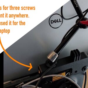 May include: A black metal laptop stand with a red lever and a cable lock. The stand has three screw holes for mounting. The stand is attached to a laptop with the Dell logo visible. The stand has a 75mm and 100mm measurement.