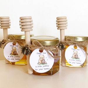 Pode incluir: Tr&ecirc;s pequenos frascos de vidro cheios de mel, cada um com um palito de mel de madeira e uma etiqueta redonda anexada. As etiquetas apresentam um personagem de desenho animado do Winnie the Pooh e o texto "Obrigado! Um pouco delicioso para sua barriga".