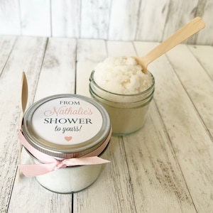 May include: Two small glass jars filled with white sugar scrub, tied with pink ribbon and a small wooden spoon. The label on the jar reads "From Nathalie's Shower to yours!"