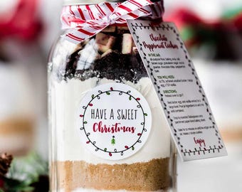 May include: A glass jar filled with layered ingredients for Chocolate Peppermint Cookies. The jar is decorated with a red and white striped ribbon and a label that says "Have a Sweet Christmas". A recipe card is attached.