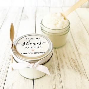 May include: A small glass jar filled with white sugar scrub, tied with a white ribbon and a label that reads "From my shower to yours Ashley's Shower".