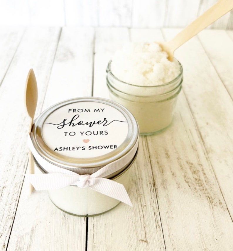 May include: A small glass jar filled with white sugar scrub, tied with a white ribbon and a label that reads "From my shower to yours Ashley's Shower".