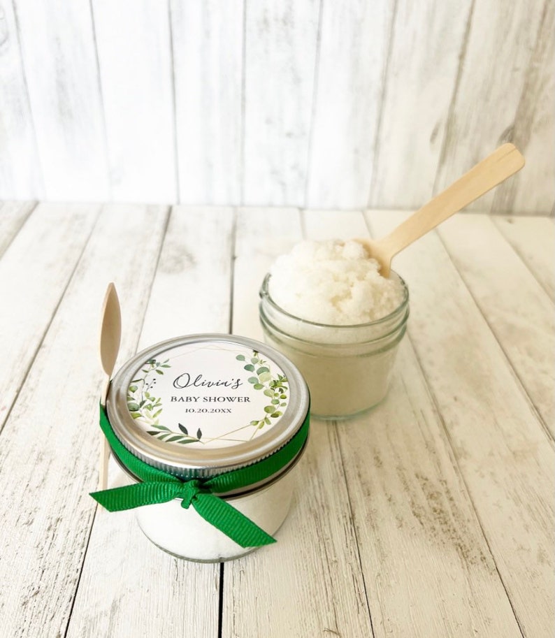 May include: A small glass jar filled with white bath salts, tied with a green ribbon and a personalised label that reads "Olivia's Baby Shower 10.20.20XX".