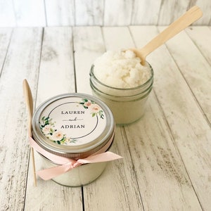 May include: Two small glass jars filled with white sugar scrub, tied with pink ribbon and labelled with a floral design and the text "Lauren and Adrian".