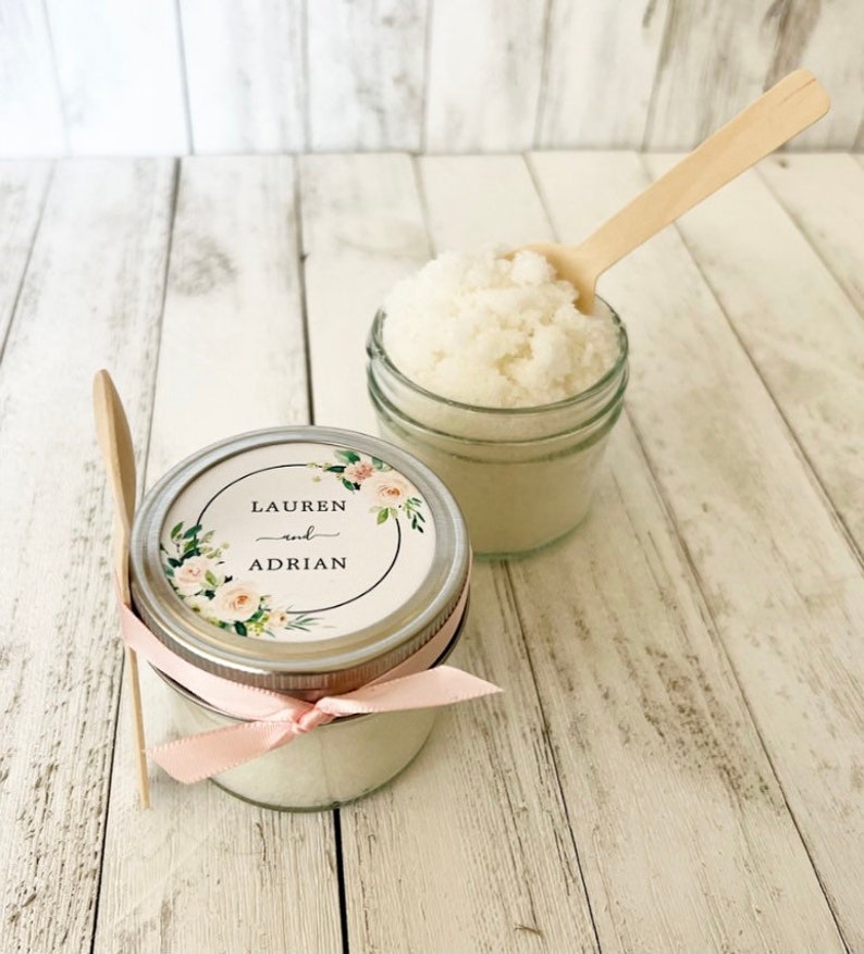 May include: Two small glass jars filled with white sugar scrub, tied with pink ribbon and labelled with a floral design and the text "Lauren and Adrian".