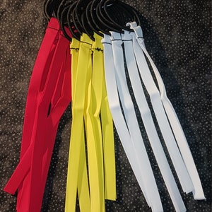 May include: A set of hair ties with fabric streamers in red, yellow, and white. The hair ties are black and are bundled together.
