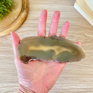 May include: A light brown agate slice with a white and green pattern. The agate is smooth and polished.