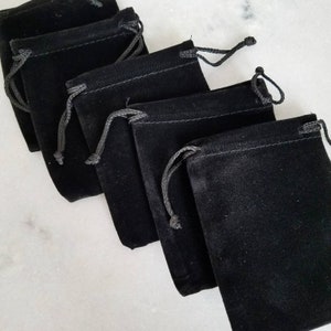 May include: Five black velvet drawstring pouches, stacked on top of each other. The pouches are made of soft, smooth fabric and have a subtle sheen.