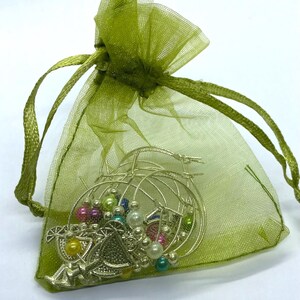 May include: A sheer lime green organza drawstring pouch containing several silver-toned hoop earrings. The earrings are decorated with small, round, multi-colored beads in shades of yellow, pink, blue, and white, along with silver metal charms.