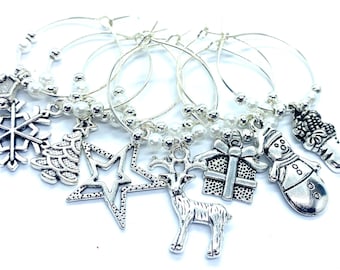 May include: A set of silver-toned metal wine glass charms featuring holiday-themed pendants including a snowflake, Christmas tree, star, reindeer, gift box, snowman, and stocking, accented with small white beads on circular wire hoops.