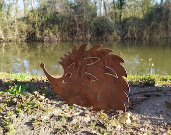 May include: A rusty metal hedgehog sculpture with a whimsical design. The sculpture is placed on a bed of brown dirt and green plants.