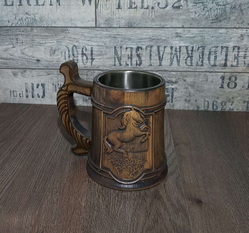 May include: A wooden beer stein with a stainless steel liner. The stein features a carved image of a horse with the words "Prancing Pony" underneath.