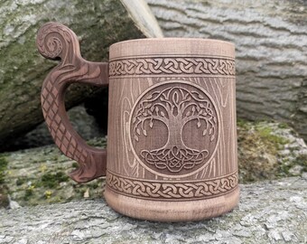 May include: A brown ceramic beer stein with a wooden-grain design. The stein features a carved Celtic knotwork tree of life design. The handle is shaped like a stylized tree branch.