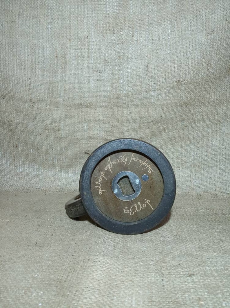 May include: A wooden bottle opener with a black metal ring around the edge. The bottle opener has the inscription "The One Ring" in Elvish script.