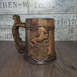 May include: A wooden beer stein with a carved horse and the words "The Prancing Pony" on the front. The stein has a brown wooden handle.
