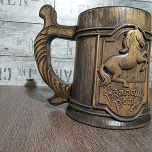 May include: A wooden beer stein with a brown and gold finish. The stein features a carved image of a prancing horse with the text "The Prancing Pony" below it.