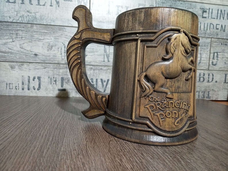 May include: A wooden beer stein with a brown and gold finish. The stein features a carved image of a prancing horse with the text "The Prancing Pony" below it.