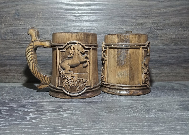 May include: Two wooden mugs, one with a carved image of a horse and the text "The Prancing Pony", the other with a carved design.