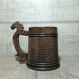 Pu&ograve; includere: Un boccale di birra in legno marrone con un manico a forma di drago. Il boccale &egrave; decorato con un motivo a scaglie.