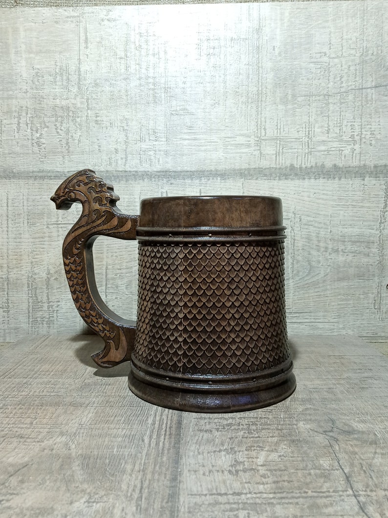 Pu&ograve; includere: Un boccale di birra in legno marrone con un manico a forma di drago. Il boccale &egrave; decorato con un motivo a scaglie.
