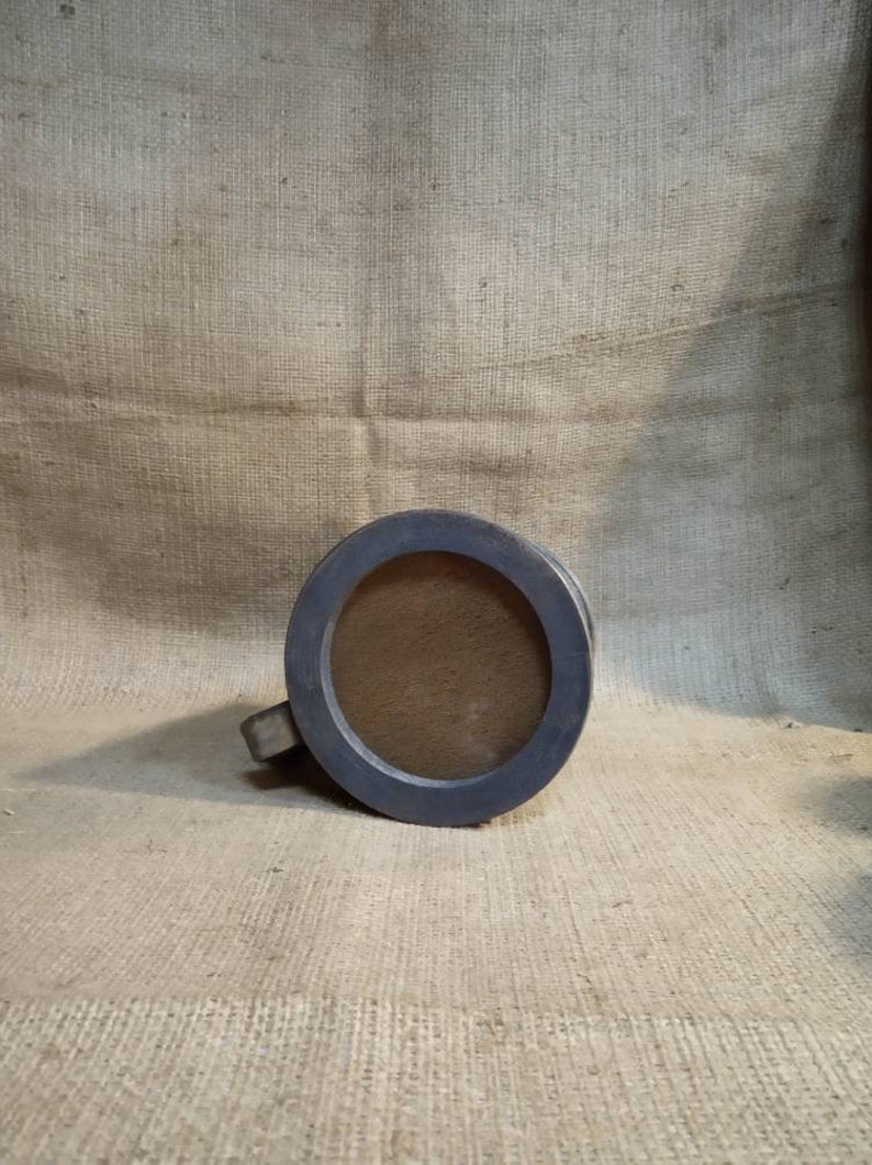 May include: A gray wooden mug with a round opening and a handle. The mug is sitting on a burlap surface.