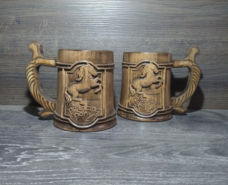 May include: Two wooden beer mugs with a brown stain. Each mug features a carved image of a horse with the text "The Prancing Pony" below it.