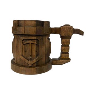 May include: A wooden beer stein with a carved handle and a shield design. The shield features a stylized sword and a letter "T".