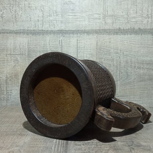 Pu&ograve; includere: Una tazza di legno marrone scuro con un manico a forma di drago scolpito. La tazza ha una parte superiore rotonda aperta e un motivo intrecciato testurizzato attorno al corpo.