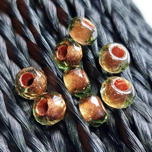 May include: Eight green glass beads with a copper metallic sheen. The beads have a hole in the center for stringing.