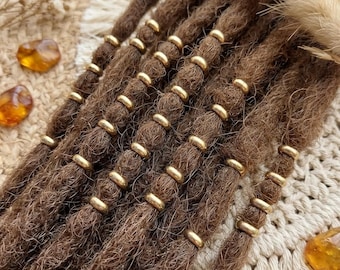 May include: A set of brown synthetic dreadlocks adorned with small, polished gold-colored metal beads spaced evenly along each strand. The textured, fibrous locks are arranged in parallel rows, creating a uniform appearance with metallic accents.