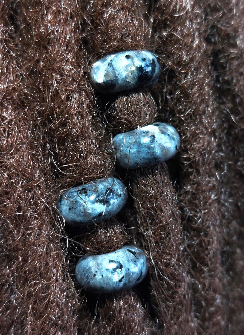 Op de afbeelding: Vier blauwgrijze edelsteen kralen met een gevlekt patroon zijn geregen op bruin dreadlocks.
