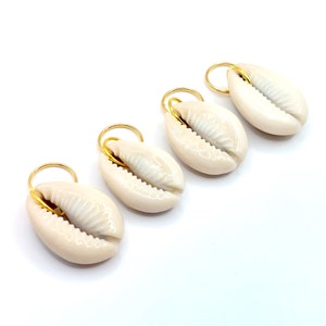 May include: Four white cowrie shells with gold rings attached. The shells are arranged in a row on a white background.