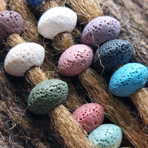 May include: Close-up of various colorful porous lava stones. The stones are in shades of blue, white, pink, green, and black. They are arranged on a textured, brown surface, possibly natural fiber.