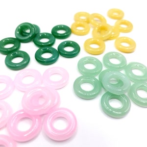 May include: Assortment of colorful donut shaped beads in pink, green, and yellow. The beads are made of glass and have a smooth, glossy finish.