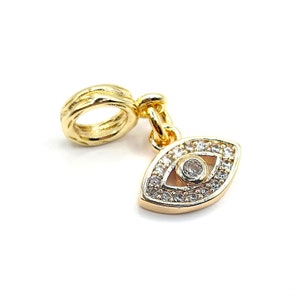 May include: Gold charm with a detailed evil eye design. The eye is surrounded by clear sparkling stones. The charm has a loop for attaching to a bracelet or necklace.