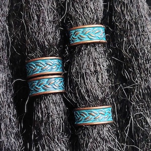 May include: Three turquoise and copper dreadlock beads with a braided pattern. The beads are on black dreadlocks.