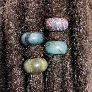 May include: Four colorful stone beads for dreadlocks. The beads are in shades of blue, green, and brown with a marbled pattern.
