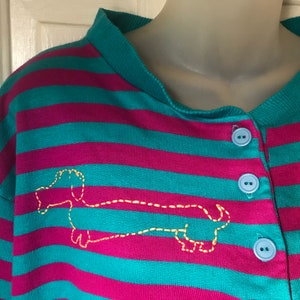 May include: Teal and magenta striped long-sleeved shirt with a yellow embroidered dachshund on the front. The shirt has a button placket.