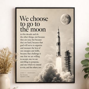 May include: A framed wall art print featuring a sepia-toned image of a rocket launching into the sky with the moon visible above. The text reads: We choose to go to the moon in this decade and do the other things, John F. Kennedy, September 12, 1962.