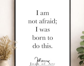 以下が含まれることがあります： 黒い文字で「I am not afraid; I was born to do this.」と書かれた額装されたウォールアートプリント。引用の下には、スタイリッシュな署名と「Joan of Arc」という名前が白い背景に黒い文字で記されており、細い黒いフレームに収められています。