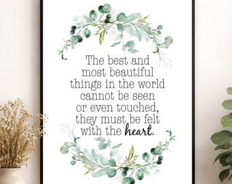 Può includere: Una stampa artistica rettangolare da parete in una cornice nera con il testo: The best and most beautiful things in the world cannot be seen or even touched, they must be felt with the heart. La citazione è circondata da una ghirlanda di eucalipto ad acquerello.