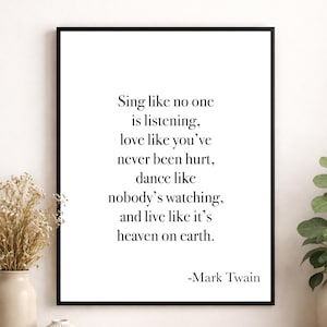 May include: A framed print with a black border displaying a Mark Twain quote in a minimalist style. The text, in a simple font, reads: "Sing like no one is listening..." The print is displayed near a vase with dried flowers.