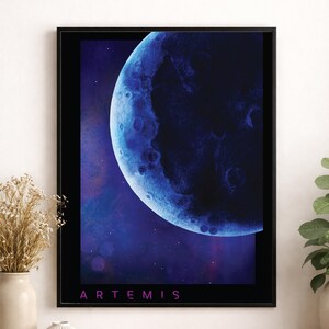 May include: A framed art print featuring a blue and purple depiction of a celestial body, possibly a moon or planet. The artwork has a dark background with the word "ARTEMIS" in pink at the bottom. The image is framed in a black border.
