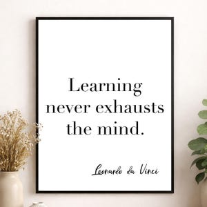 May include: A rectangular wall art print in a thin black frame featuring the black text "Learning never exhausts the mind." followed by the signature "Leonardo da Vinci" in a cursive script font against a plain white background.
