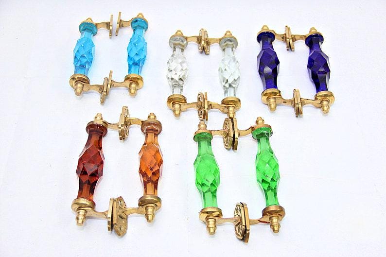 May include: Set of ten glass cabinet door pulls with brass hardware. The pulls are in various colors, including blue, green, clear, and amber.