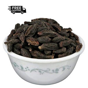 May include: A white bowl filled with dark brown, oblong-shaped dried fruit. The bowl has a decorative floral pattern around the rim. The fruit appears to be a natural product, possibly a type of dried nut or seed.