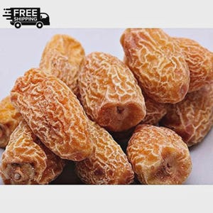 Puede incluir: Primer plano de un montón de dátiles secos. Los dátiles son de color marrón claro y tienen una textura arrugada. La imagen está bien iluminada, mostrando los dátiles en detalle. Los dátiles son un snack popular.