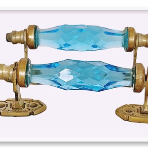 May include: Two antique glass door handles with brass fixtures. The handles are faceted and have a light blue color.